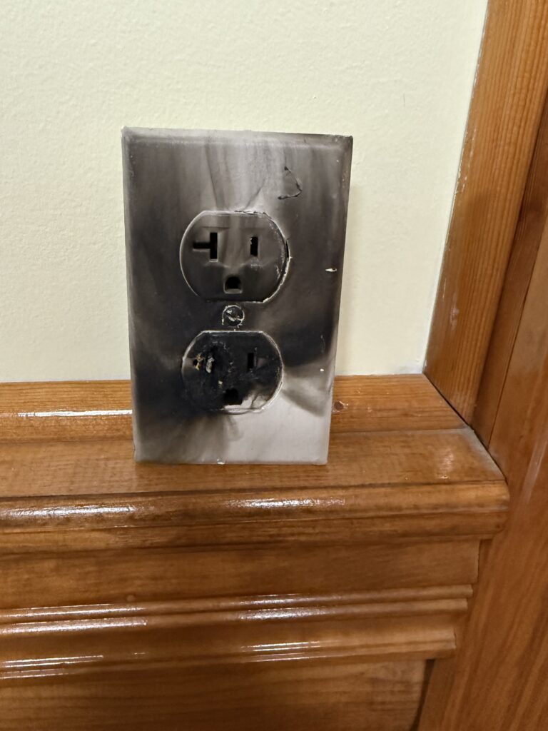 A burnt, scorched electrical outlet showing heat damage, a fire hazard that signals the need for an electrician.