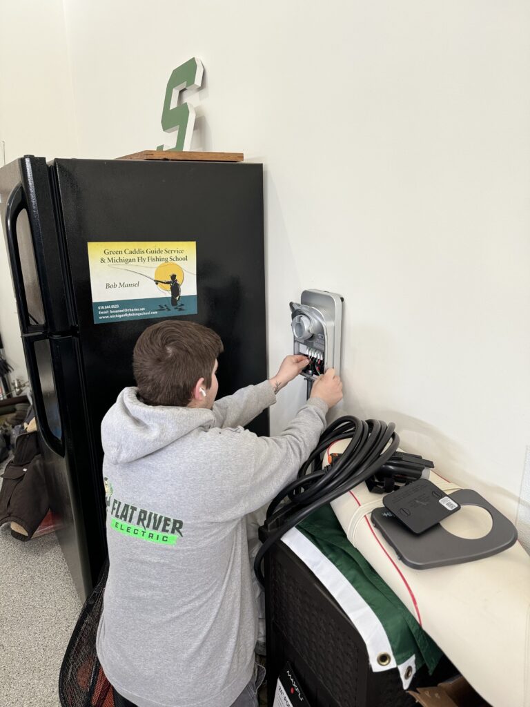 Flat River Electric technician installing a Level 2 ChargePoint EV charger on a garage wall in a West Michigan home.