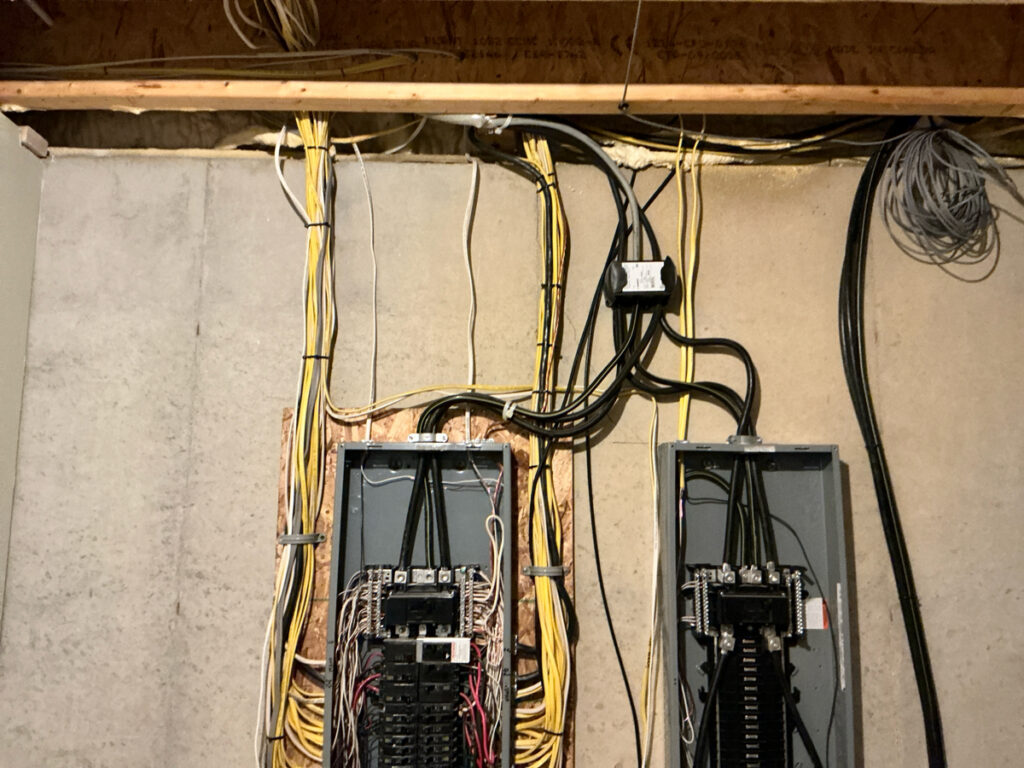 Before photo of an outdated, overcrowded electrical panel with tangled wiring in a West Michigan home, ready for replacement.